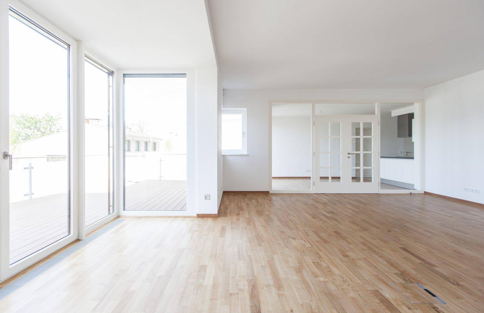 Lichtdurchfluteter Wohnraum mit Holzboden und breiten Schiebetüren zur Außenterrasse.