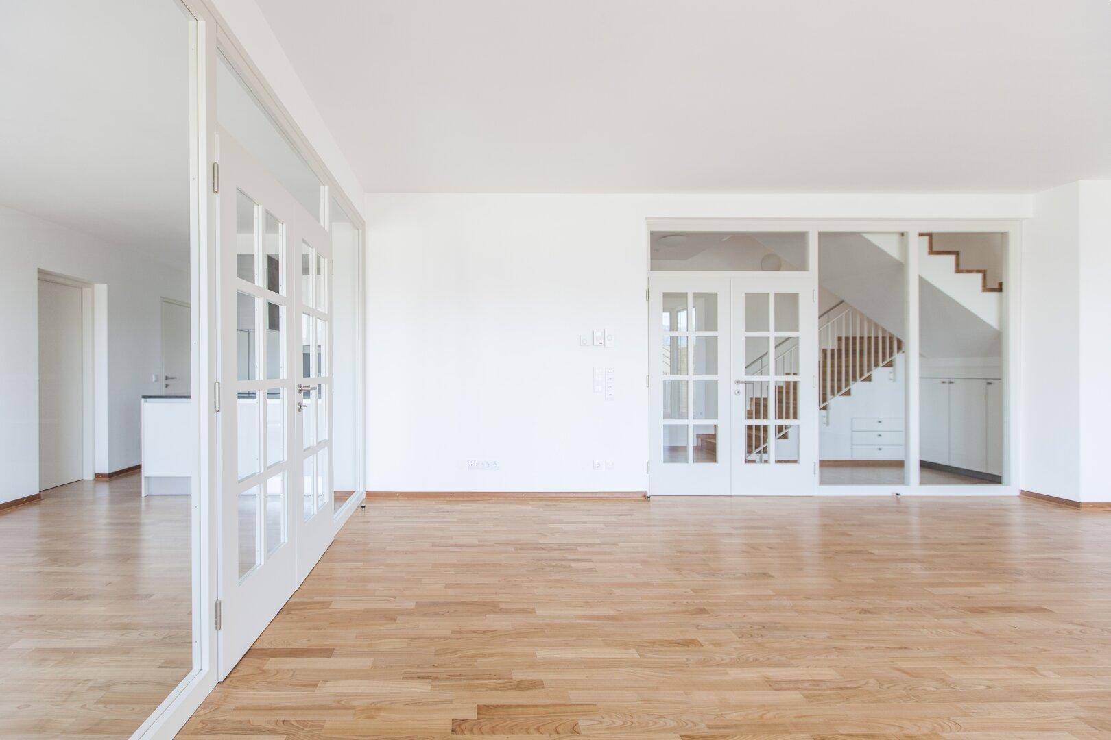 Geräumiger Wohnbereich mit Holzboden, viel Tageslicht und Blick auf die Treppe.