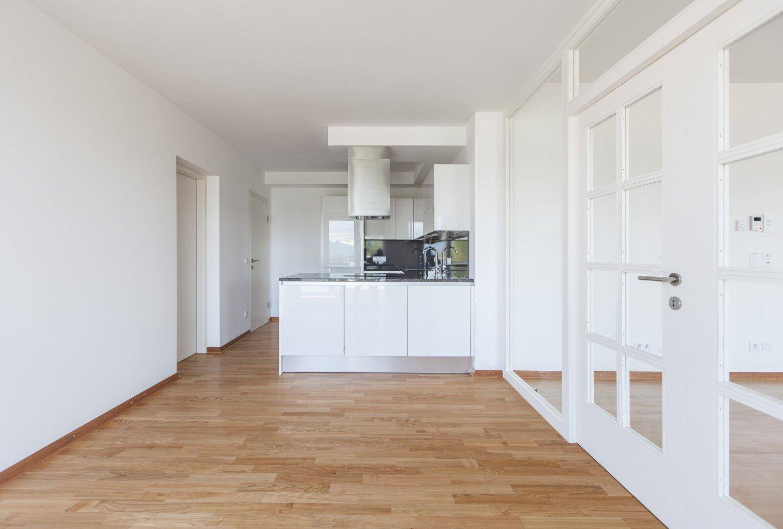 Moderne, offene Küche mit weißen Hochglanzschränken und dunkler Arbeitsplatte.