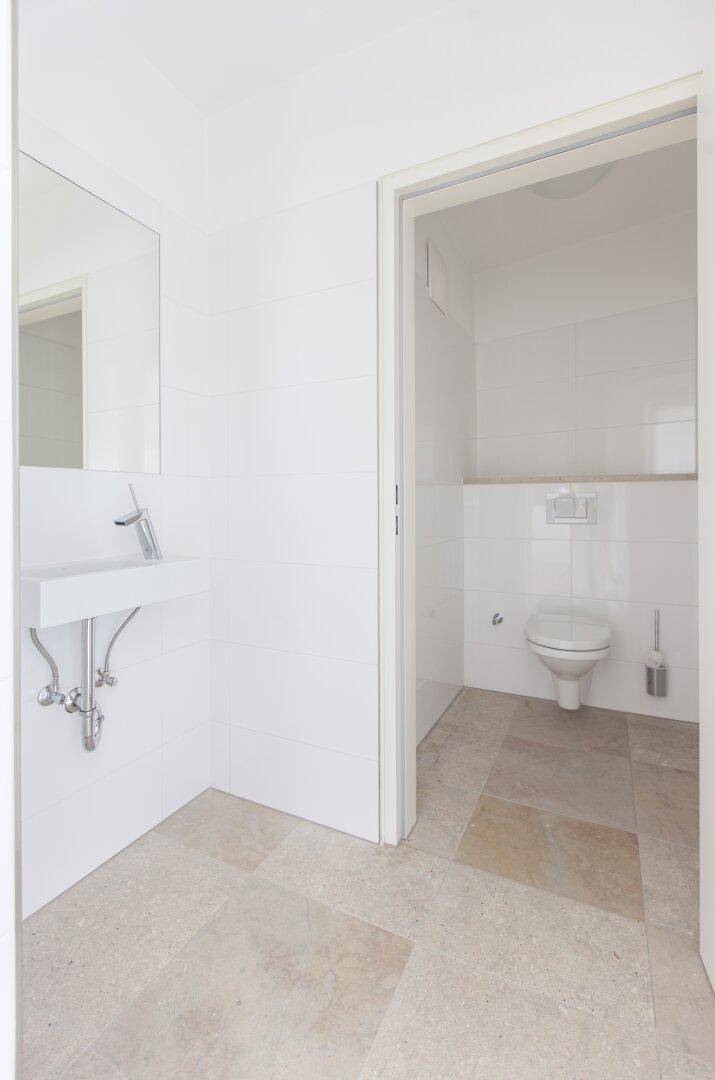 Modernes Gäste-WC mit Wand-WC, Waschbecken und hellen Fliesen.