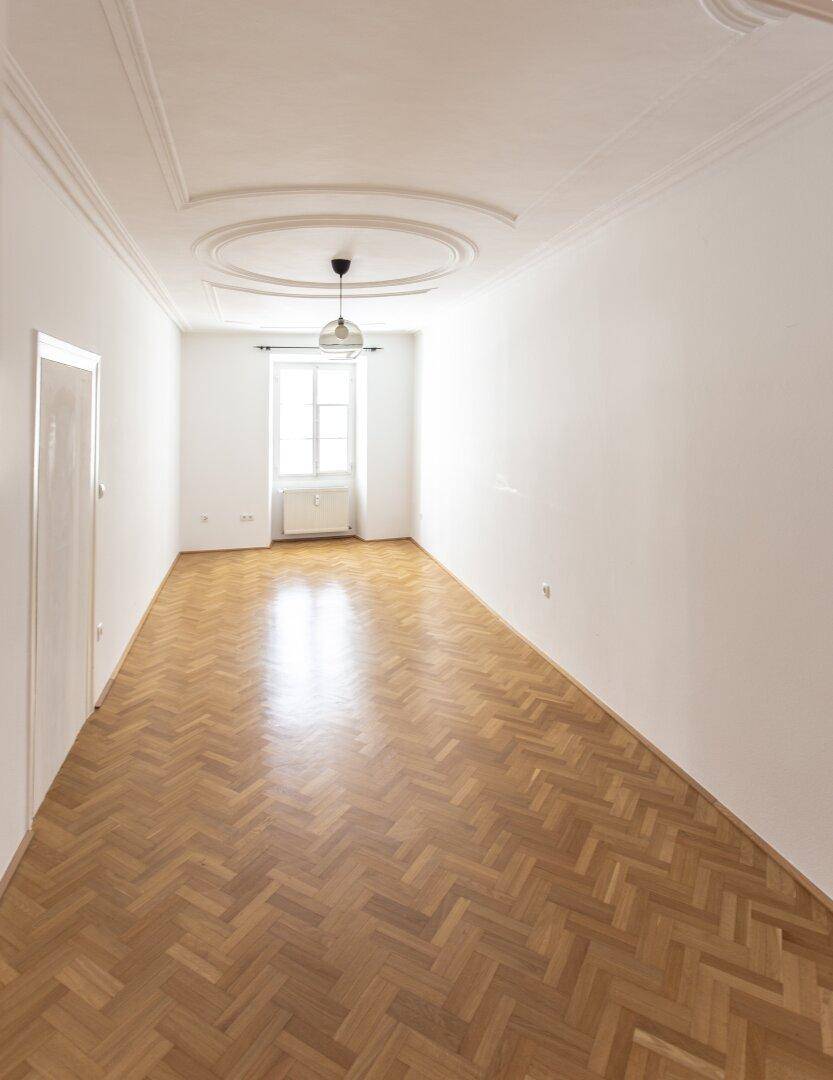 Langer, heller Raum mit Fischgrätparkett und Stuckdecke, ideal für einen Wohn- oder Essbereich.