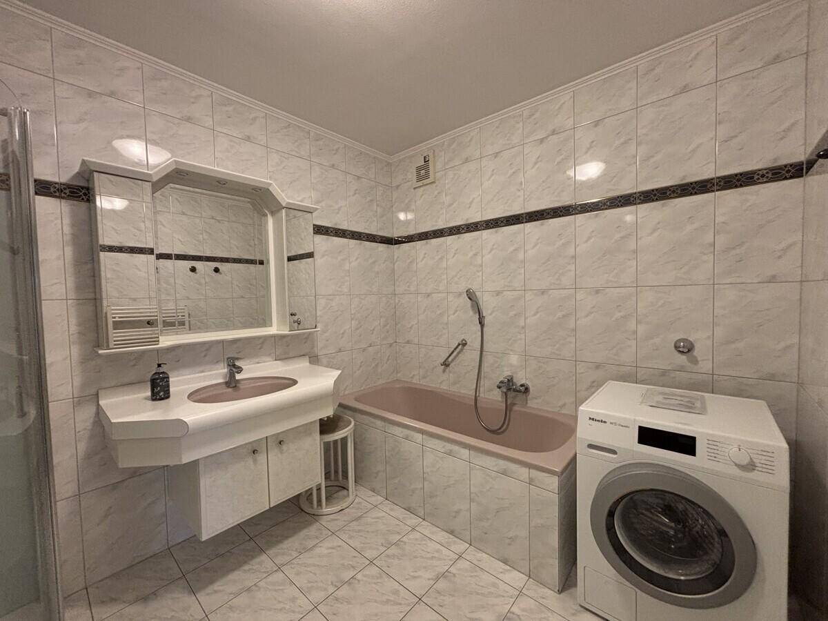 Badezimmer mit Badewanne, Waschmaschine und hellen Fliesen.