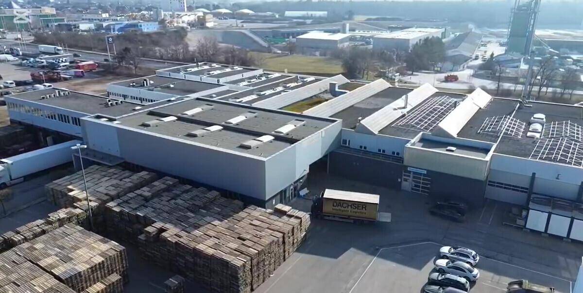 Luftaufnahme des Gewerbekomplexes mit Lastwagen, geparkten Autos und Solaranlage auf dem Dach.