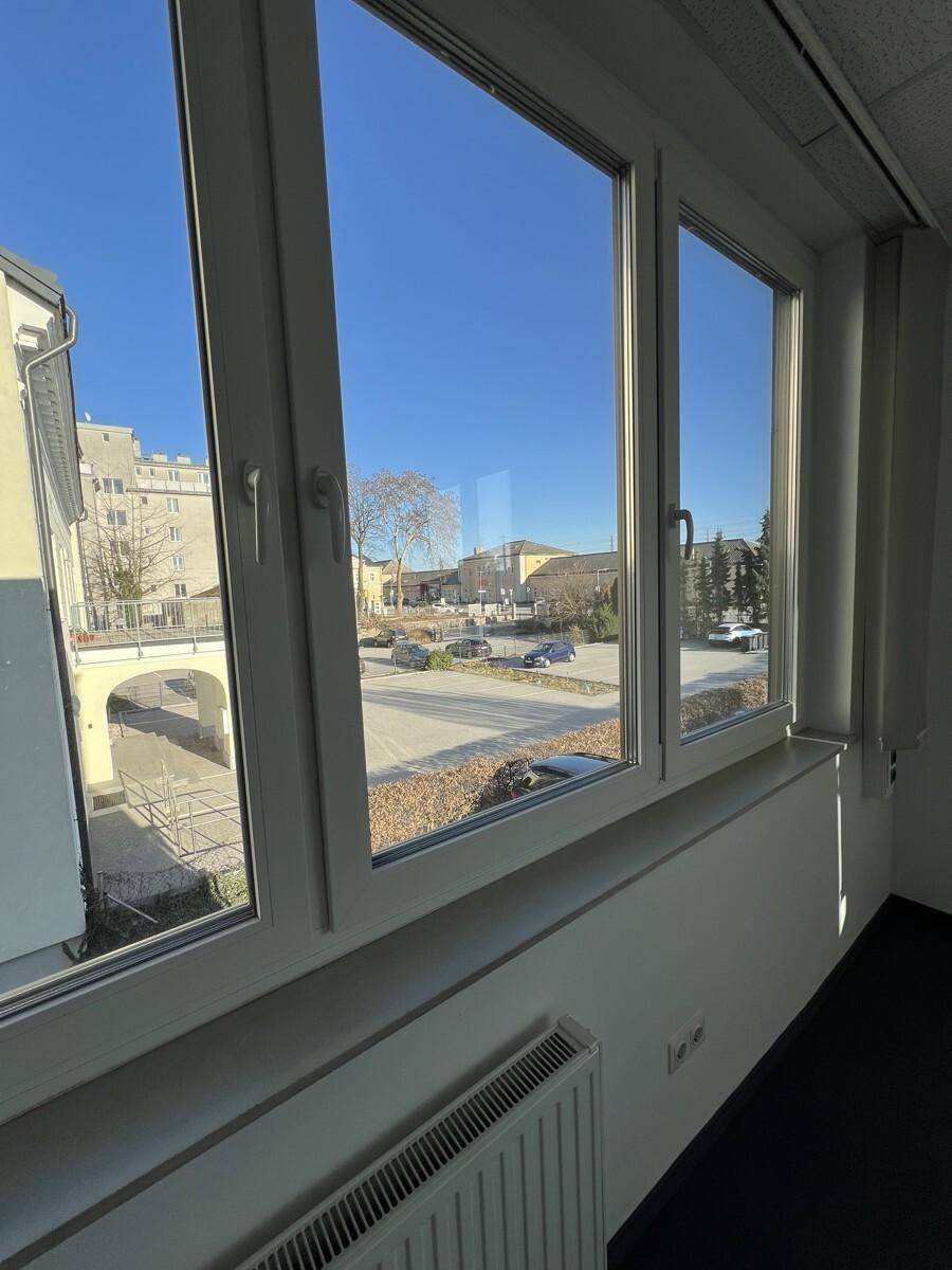 Blick aus dem Fenster auf eine belebte Straße mit parkenden Autos und umliegenden Gebäuden.