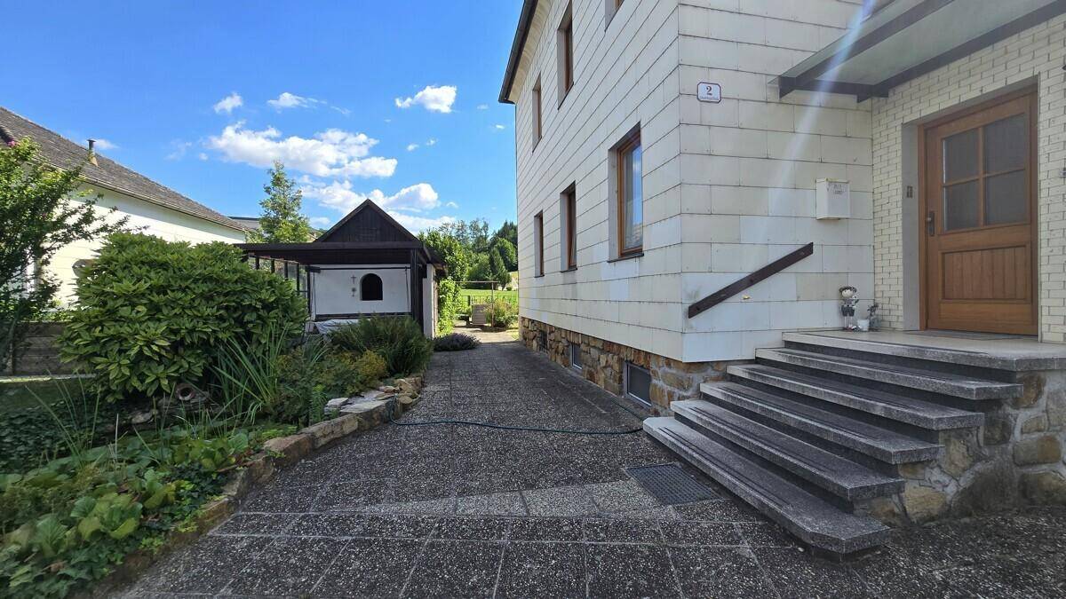 Eingangsbereich des Hauses mit Steintreppe, gepflastertem Weg und Nebengebäude.