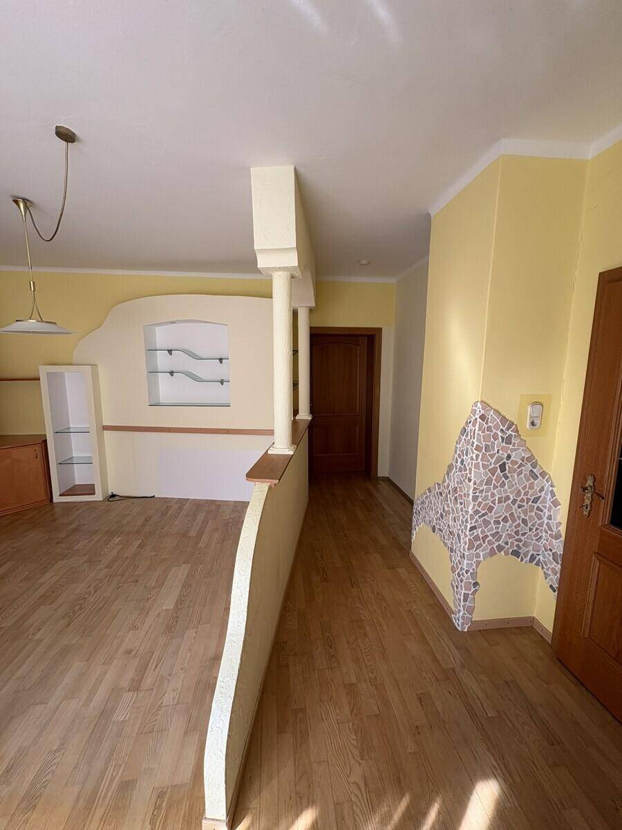 Wohnbereich mit dekorativer Halbwand, Holzboden und Zugang zu weiteren Räumen.
