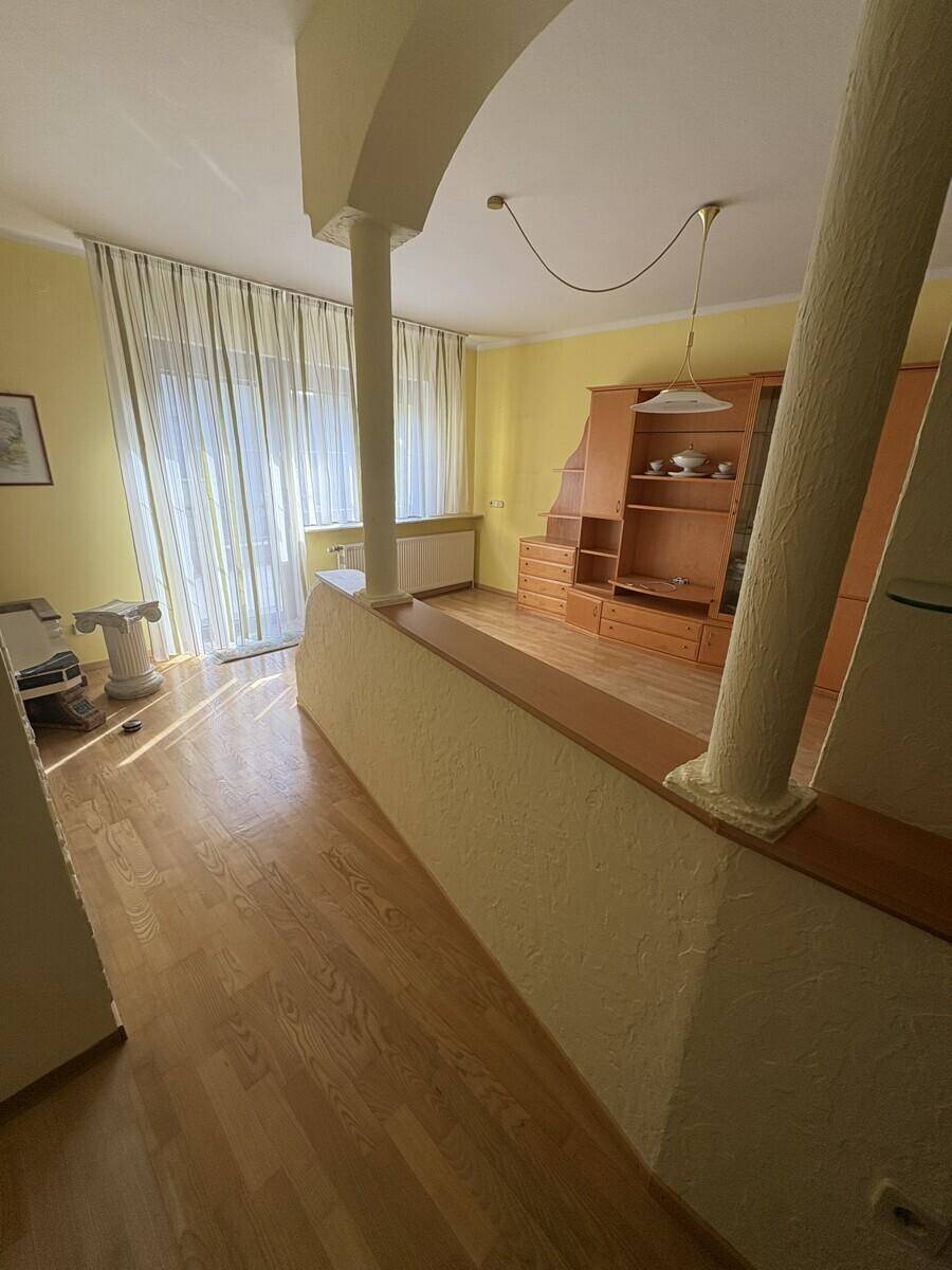 Lichtdurchfluteter Wohnraum mit Holzboden, großen Fenstern und dekorativer Säule.