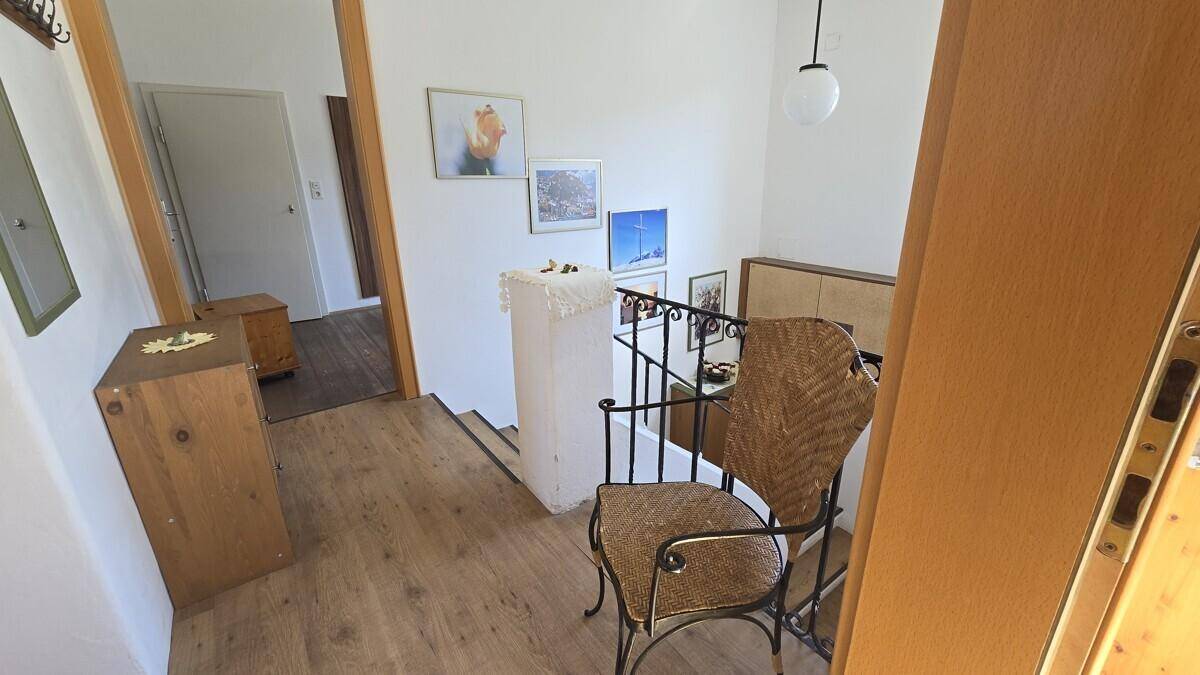 Treppenabsatz mit hellem Holzfußboden, einem Stuhl und gerahmten Bildern an der weißen Wand.