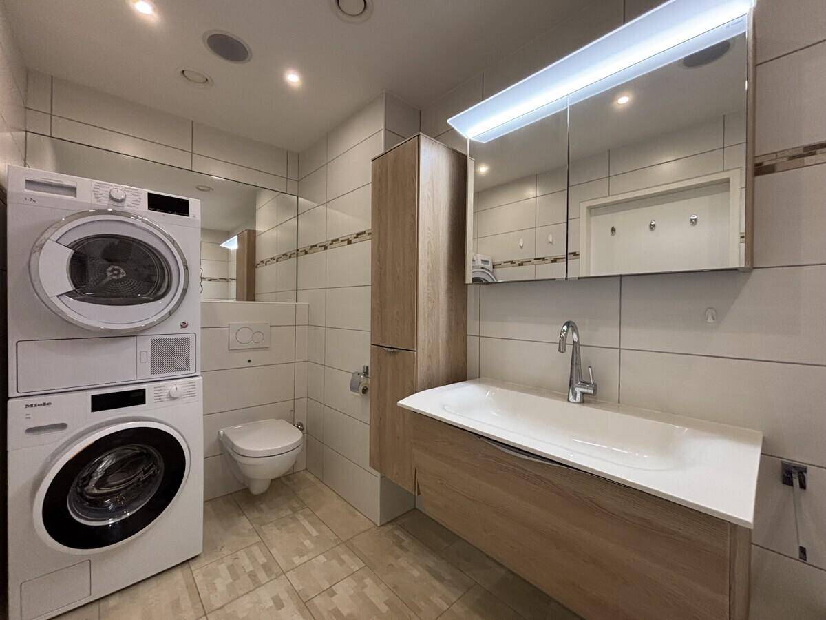 Modernes Badezimmer mit Waschmaschine, Trockner und wandhängendem WC.