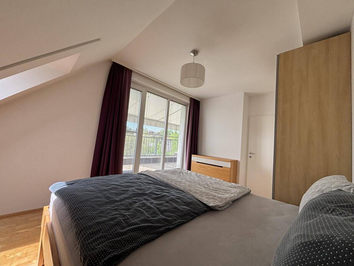 Schlafzimmer mit Bett, Holzboden und großen Fenstern zur Dachterrasse.