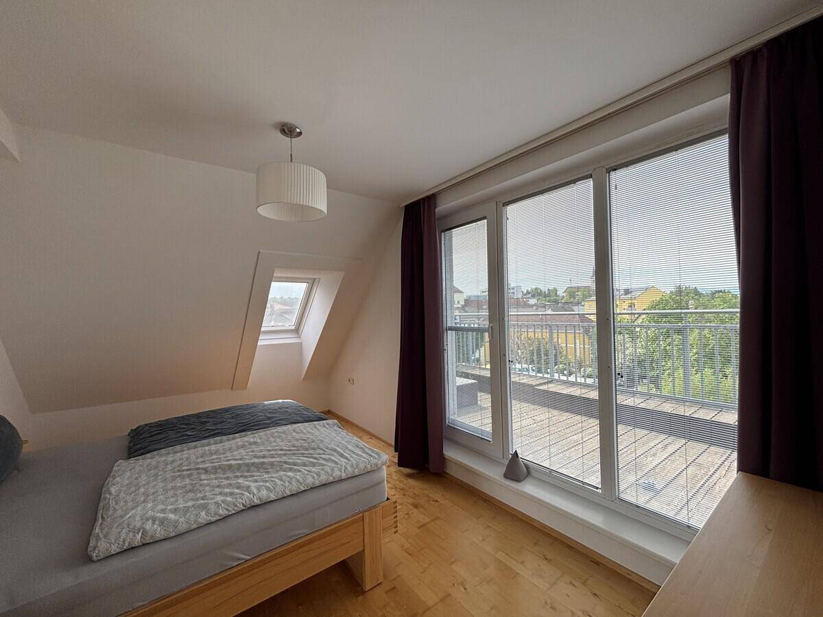 Schlafzimmer mit Bett, Holzboden und Zugang zur Dachterrasse.