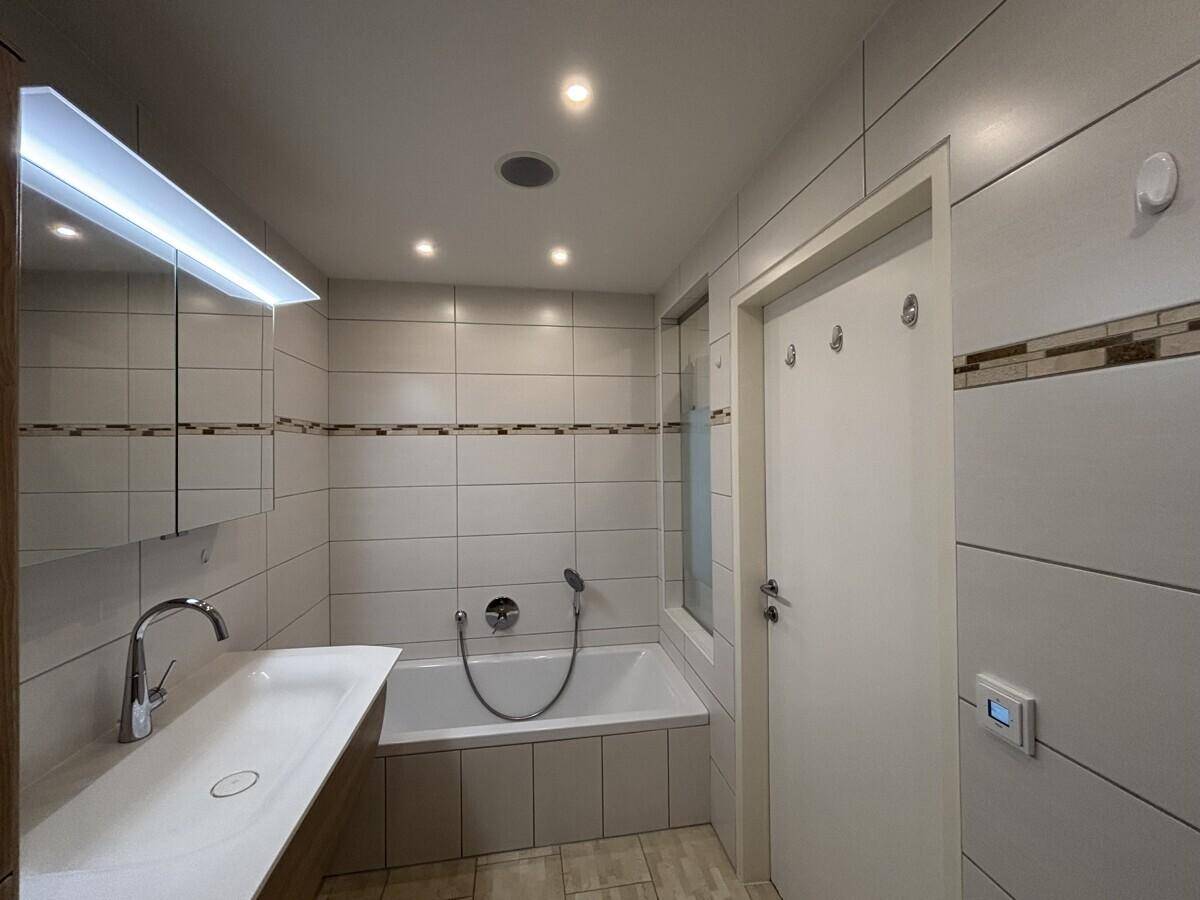 Helles Badezimmer mit Badewanne, Fliesenboden und Spiegelschrank.