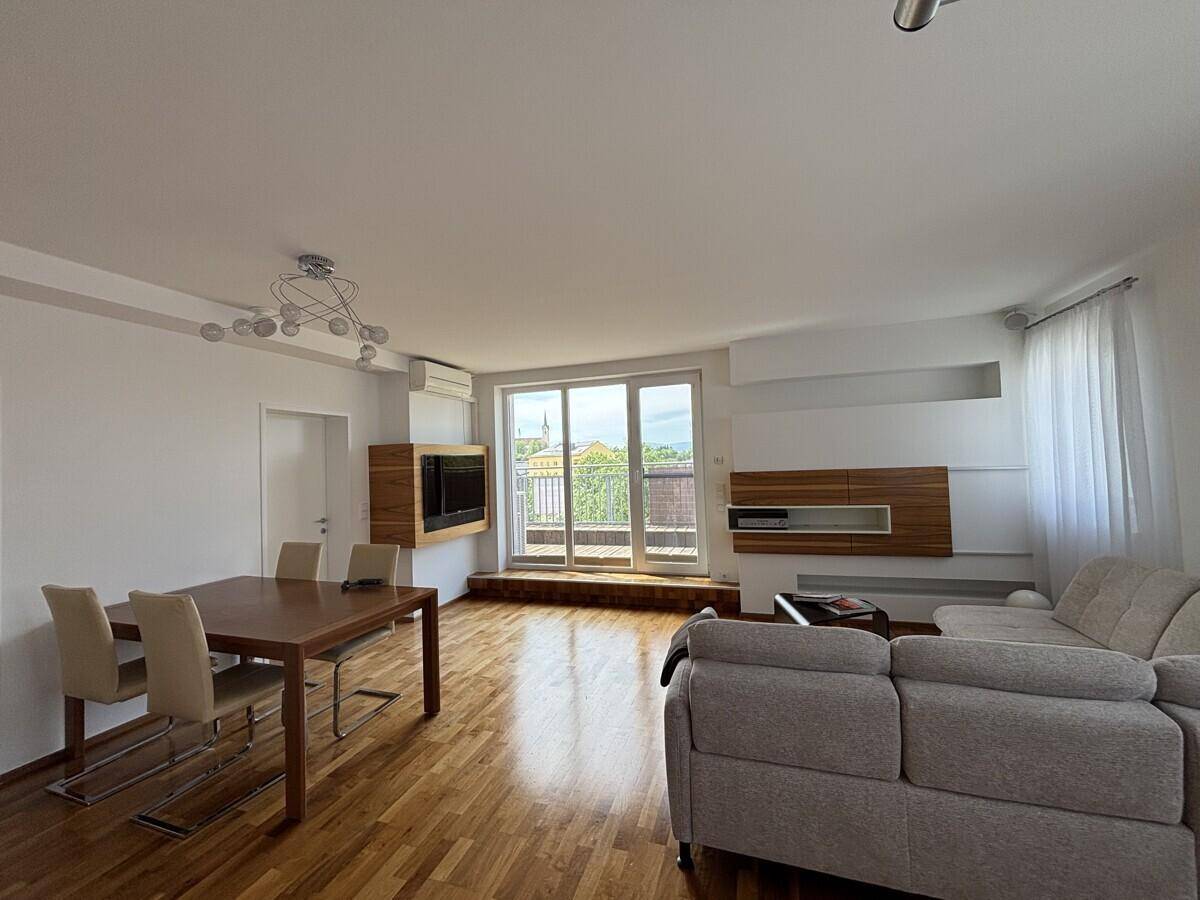 Heller Wohn-Essbereich mit Esstisch, Sofa und großen Fenstern zum Balkon.