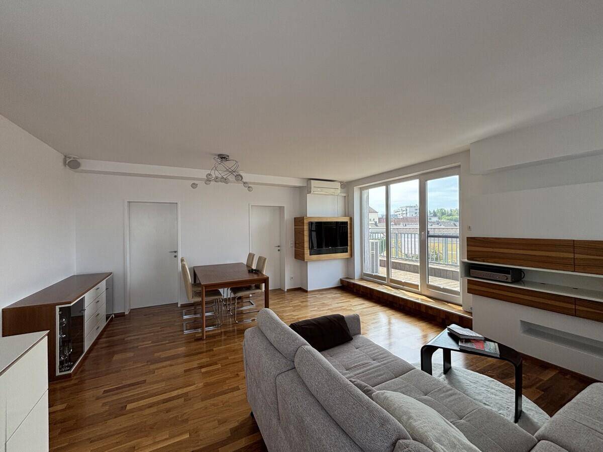Offener Wohn-Essbereich mit Sofa, Holzboden und Blick auf den Balkon.