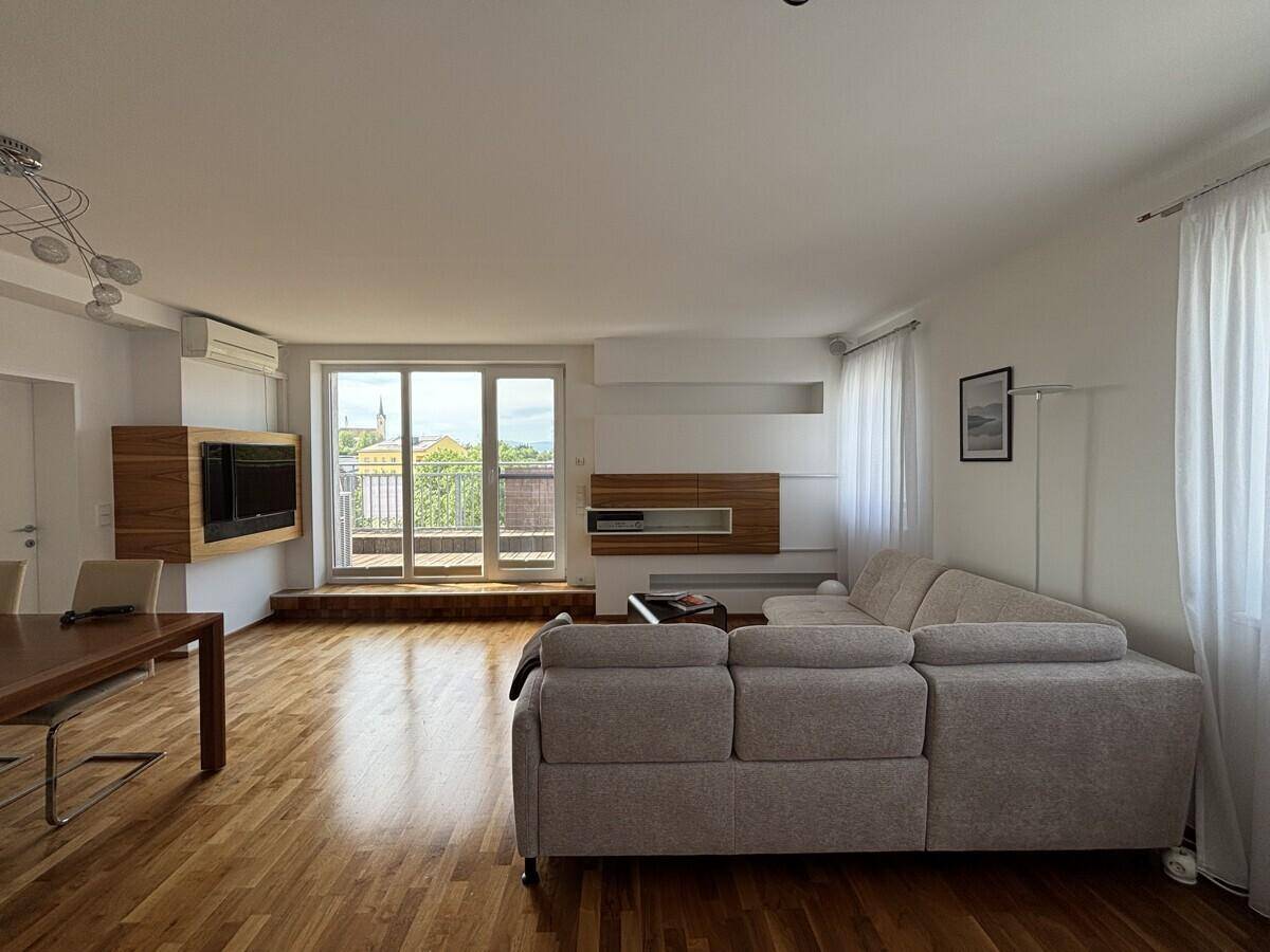 Geräumiger Wohn-Essbereich mit Holzboden, Sofa und Zugang zum Balkon.