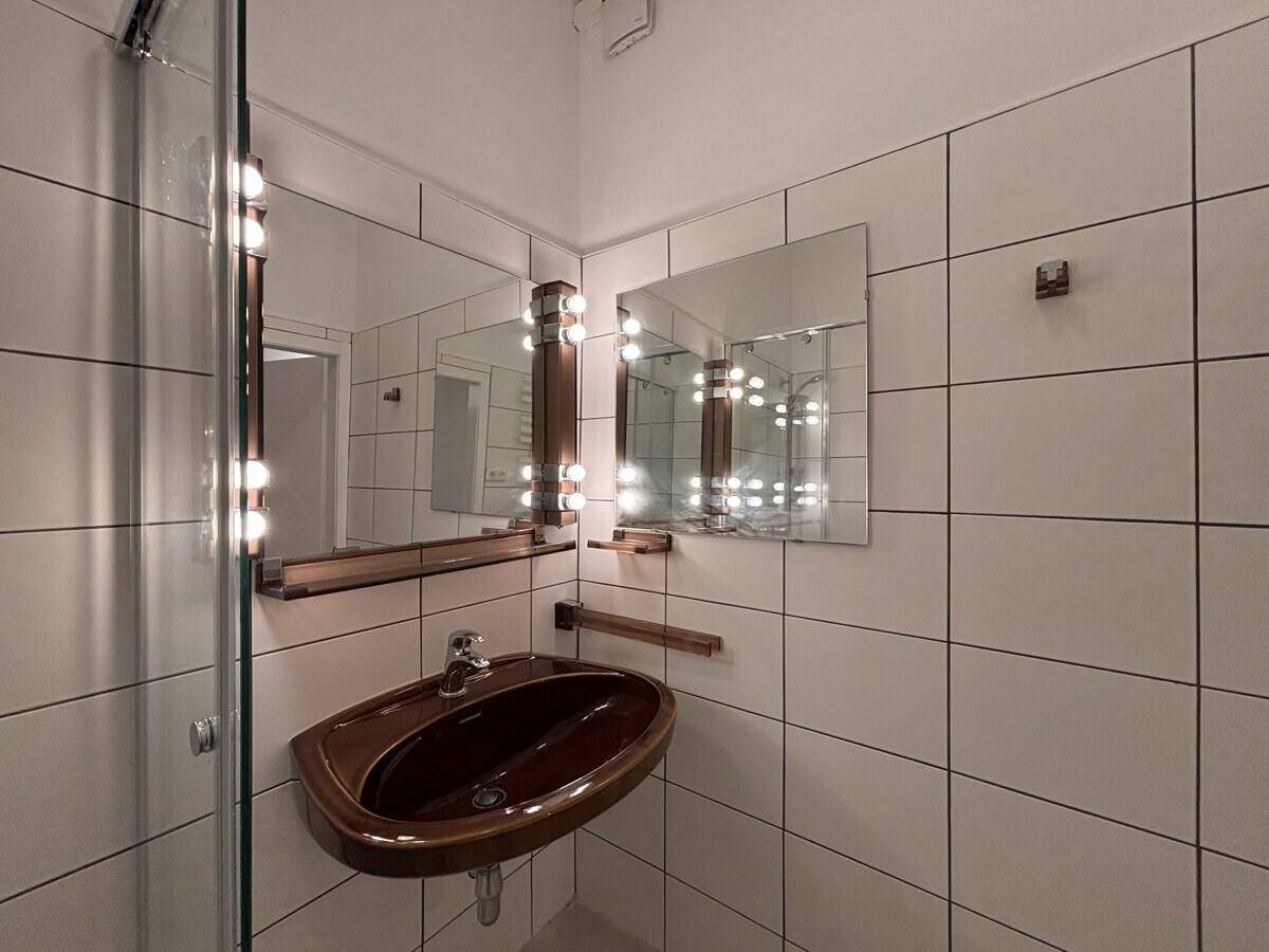 Badezimmer mit weiß gefliesten Wänden, Waschbecken und beleuchtetem Spiegel.