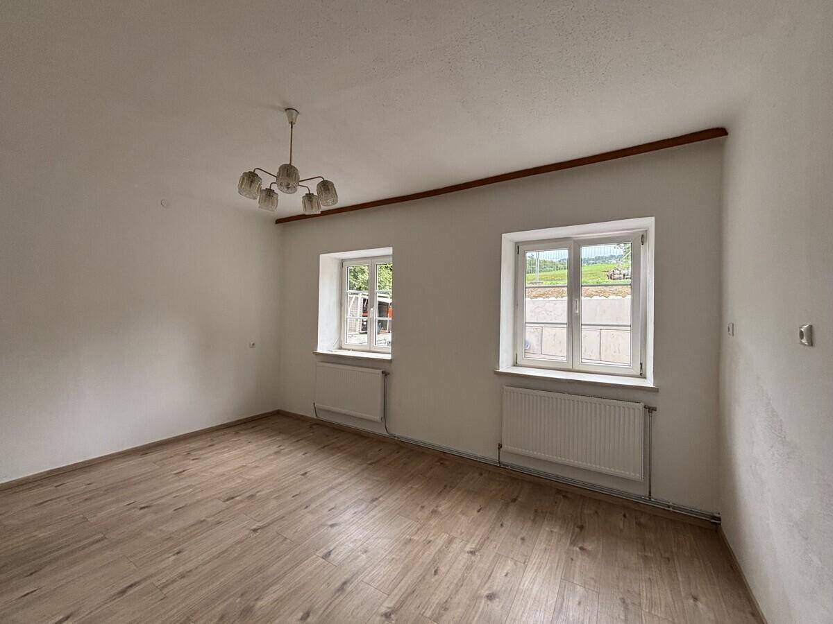 Helles Wohnzimmer mit zwei Fenstern, die einen grünen Ausblick bieten, und Laminatboden.