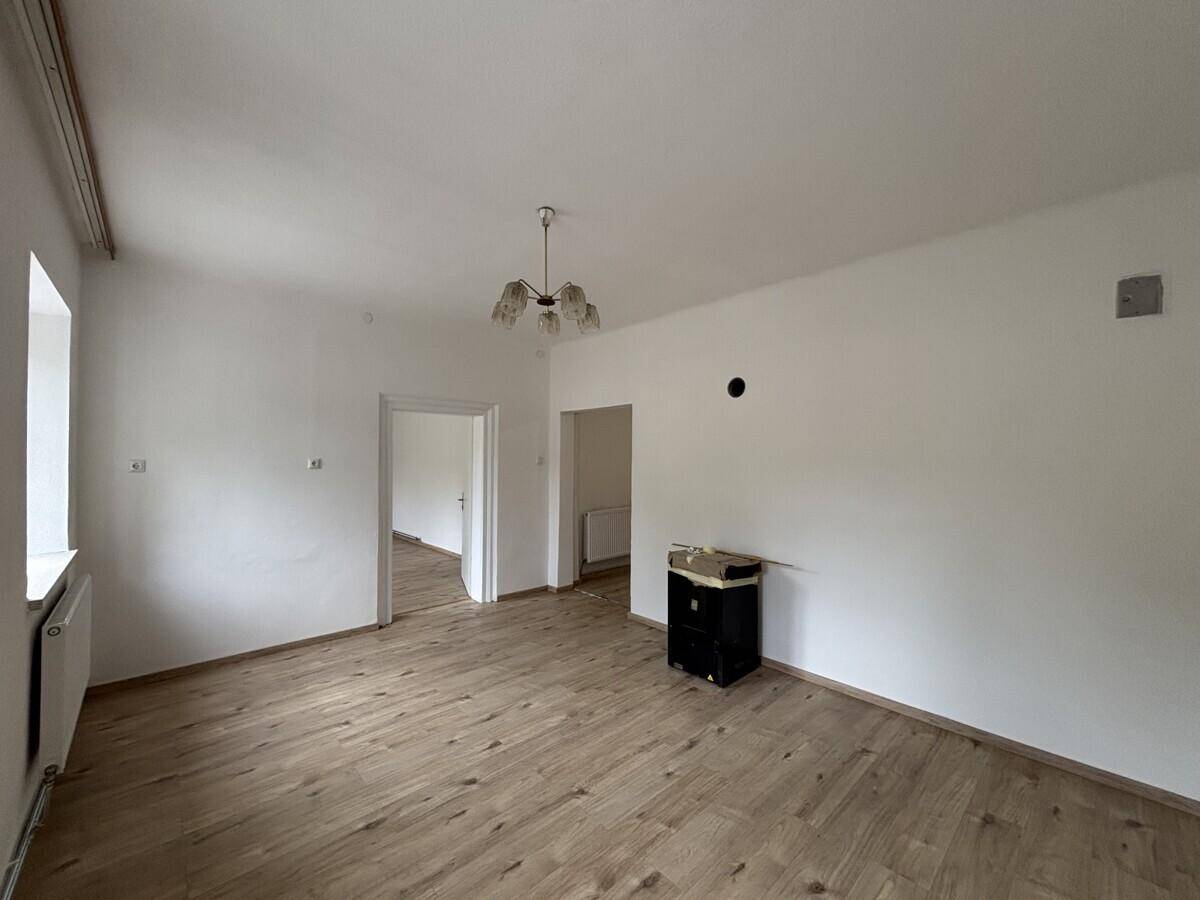 Geräumiges Wohnzimmer mit hellem Laminatboden und Zugang zu weiteren Räumen.