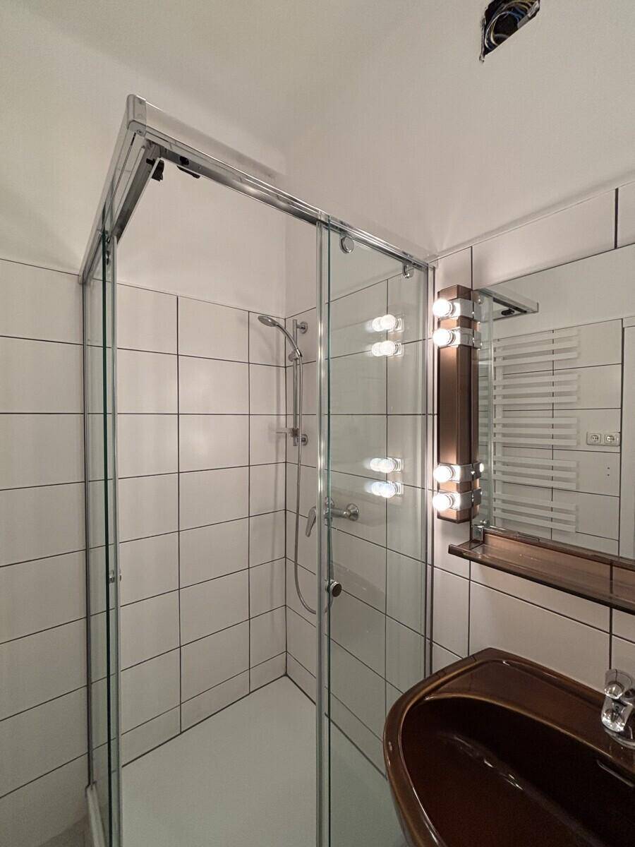 Badezimmer mit Duschkabine, Waschbecken und weiß gefliesten Wänden.