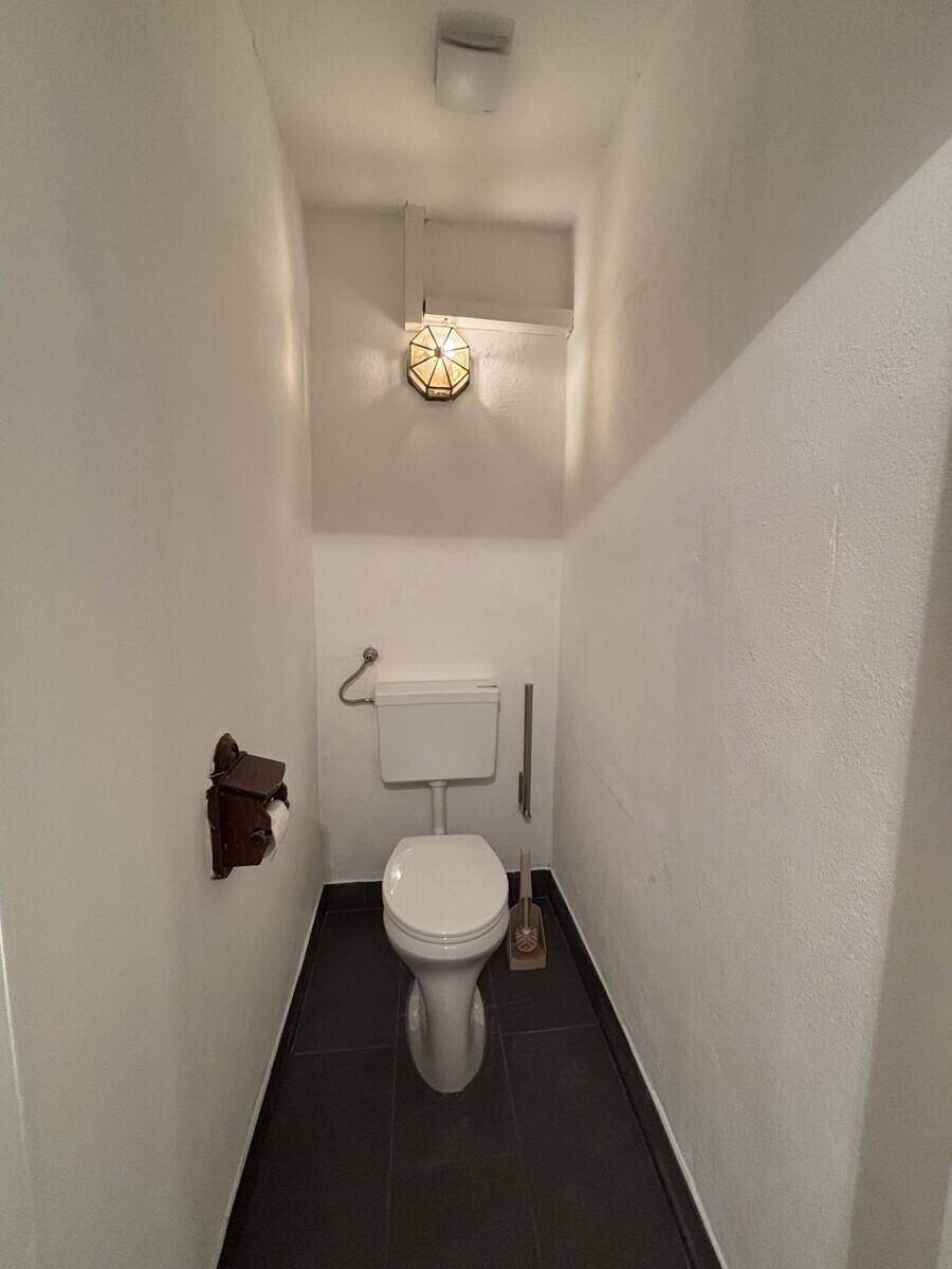 Kleines separates WC mit dunklem Fliesenboden und weißer Toilette.