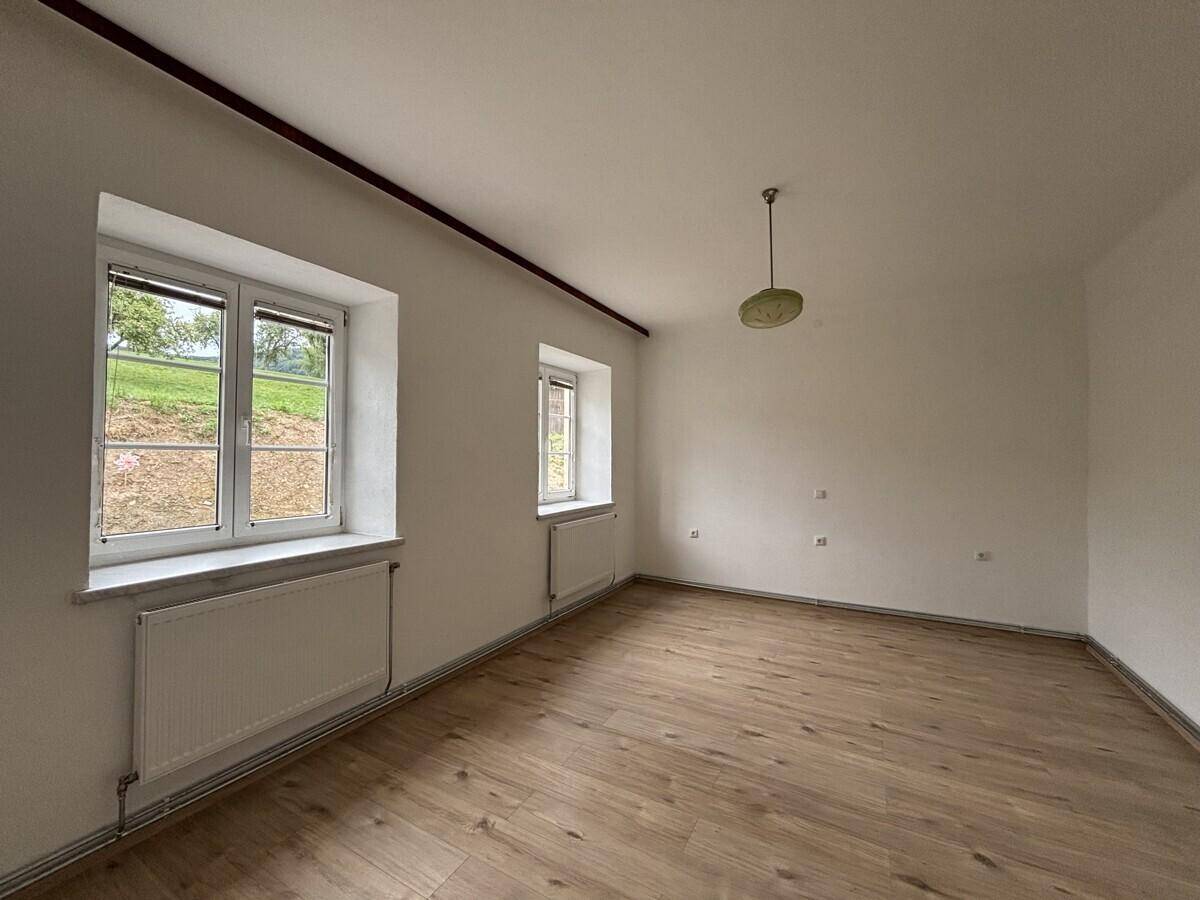 Lichtdurchflutetes Zimmer mit zwei großen Fenstern und Blick ins Grüne.