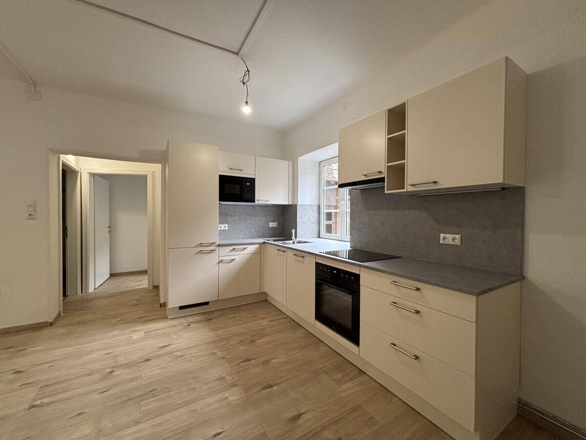 Moderne Einbauküche mit hellen Fronten, integrierten Geräten und Blick nach draußen.