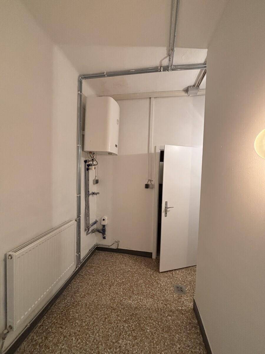 Technikraum mit Warmwasserbereiter, sichtbaren Leitungen und Terrazzoboden.