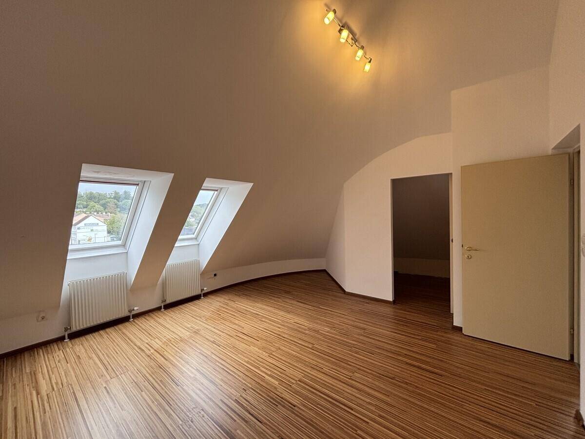 Geräumiges Dachgeschosszimmer mit Holzfußboden und mehreren Dachfenstern.