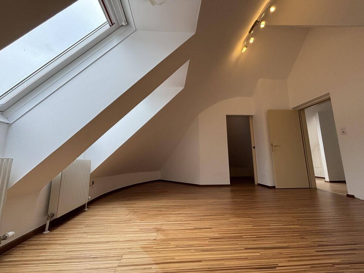 Geräumiges Dachgeschosszimmer mit Holzfußboden, großen Dachfenstern und Deckenstrahlern.