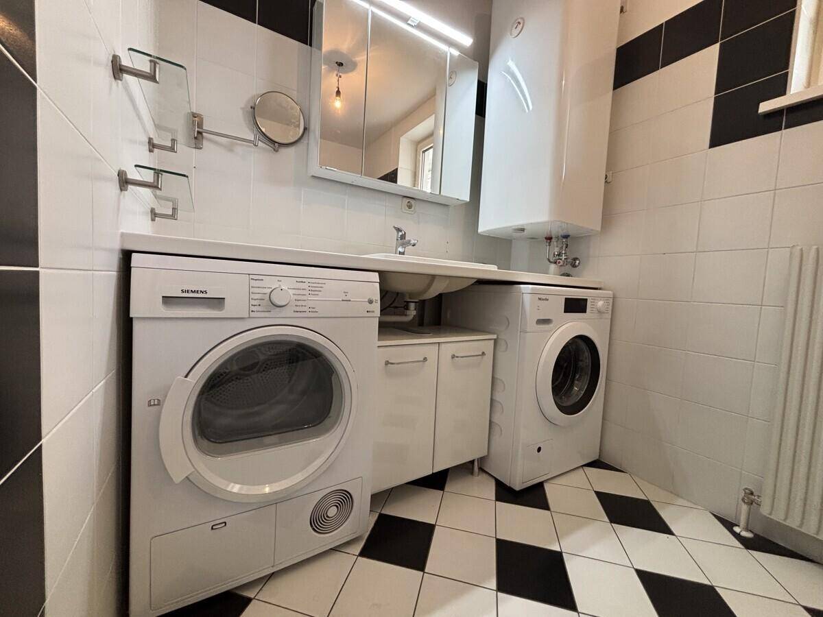 Badezimmer mit Waschmaschine, Trockner, Waschbecken und Spiegelschrank.