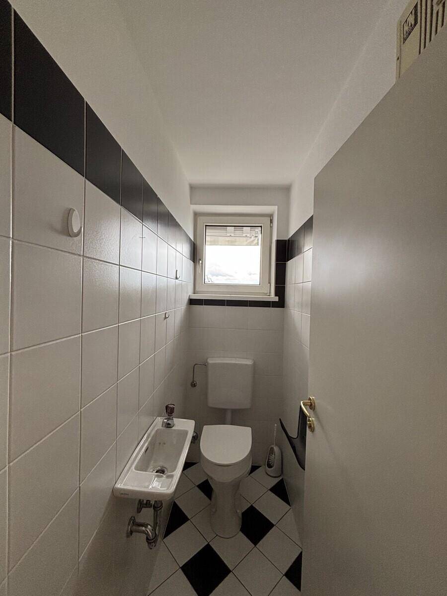 Kleines Gäste-WC mit schwarz-weißen Fliesen, Toilette, Bidet und Fenster.