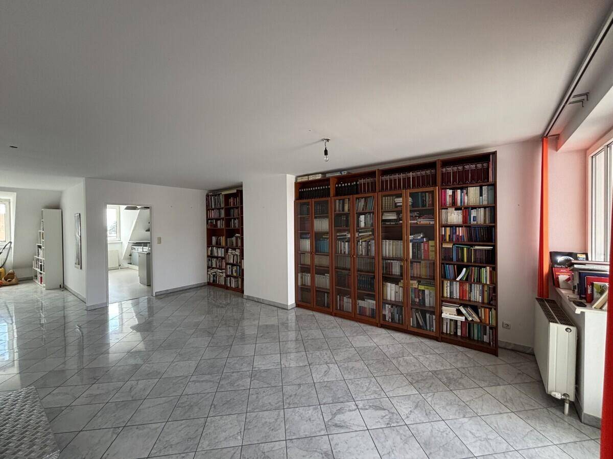 Heller Wohnbereich mit großem Bücherregal und Fliesenboden.