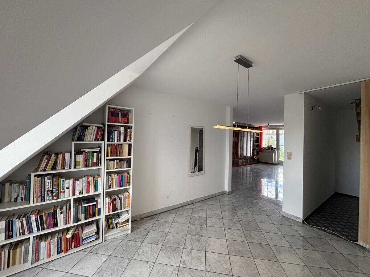 Dachgeschossraum mit Bücherregal, schrägen Wänden und Blick in den unteren Bereich.
