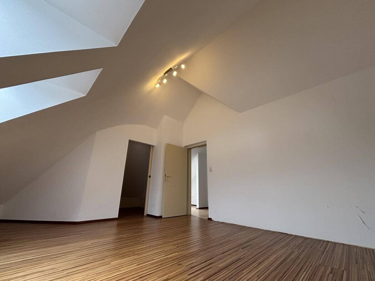 Dachgeschossraum mit Holzfußboden, schrägen Wänden und Deckenstrahlern.