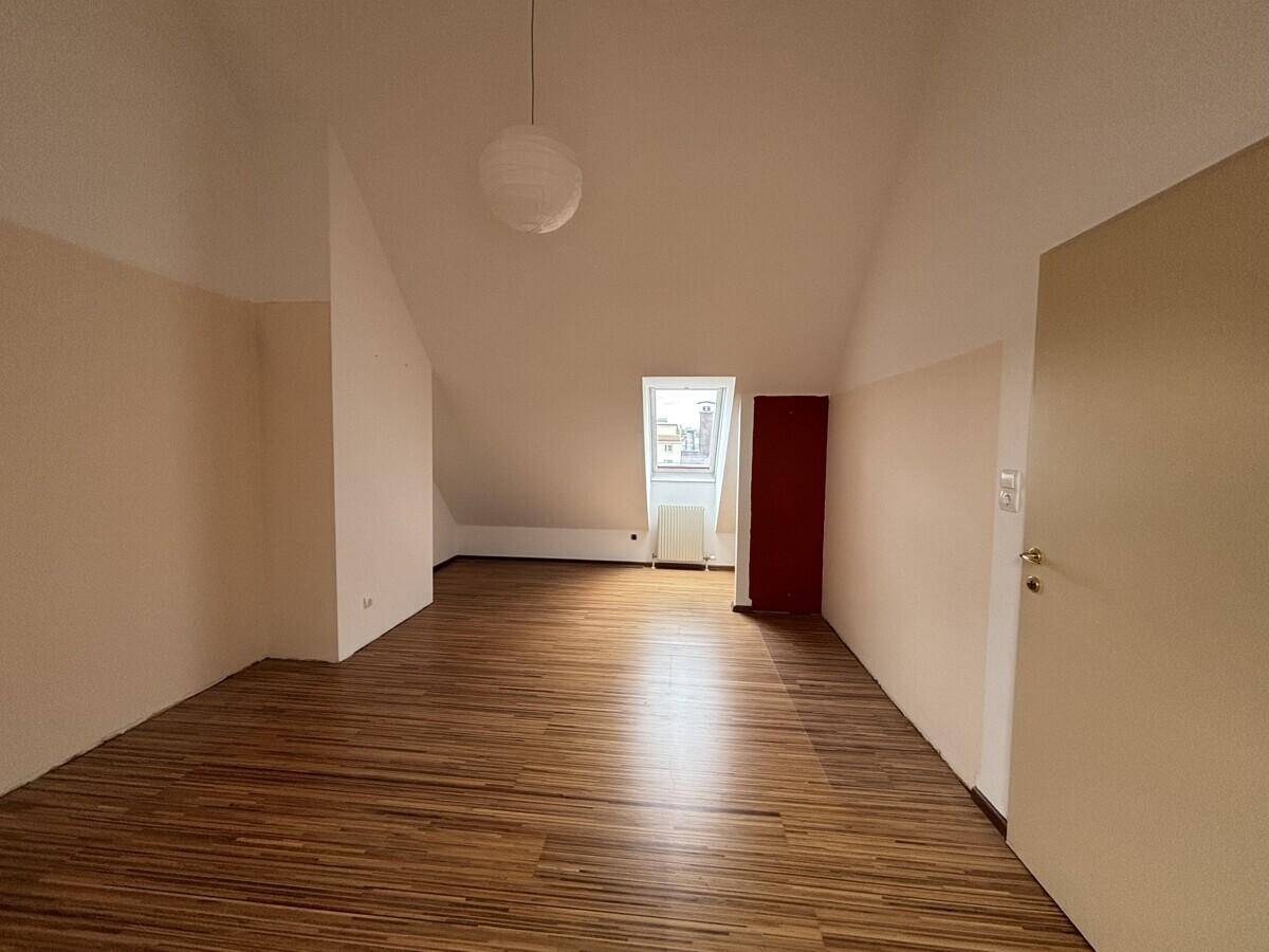 Helles Dachgeschosszimmer mit Holzfußboden, Dachfenster und schrägen Wänden.