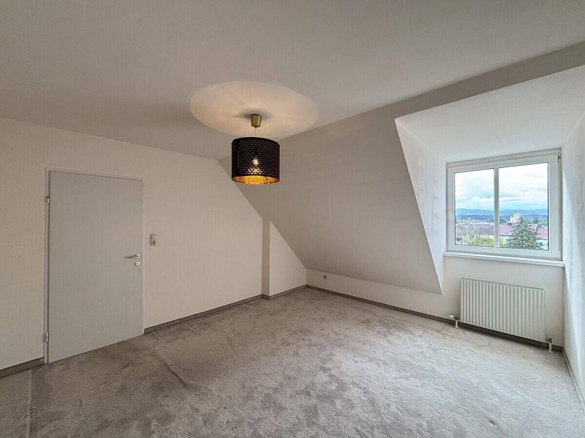 Helles Schlafzimmer im Dachgeschoss mit Teppichboden und Fenster.