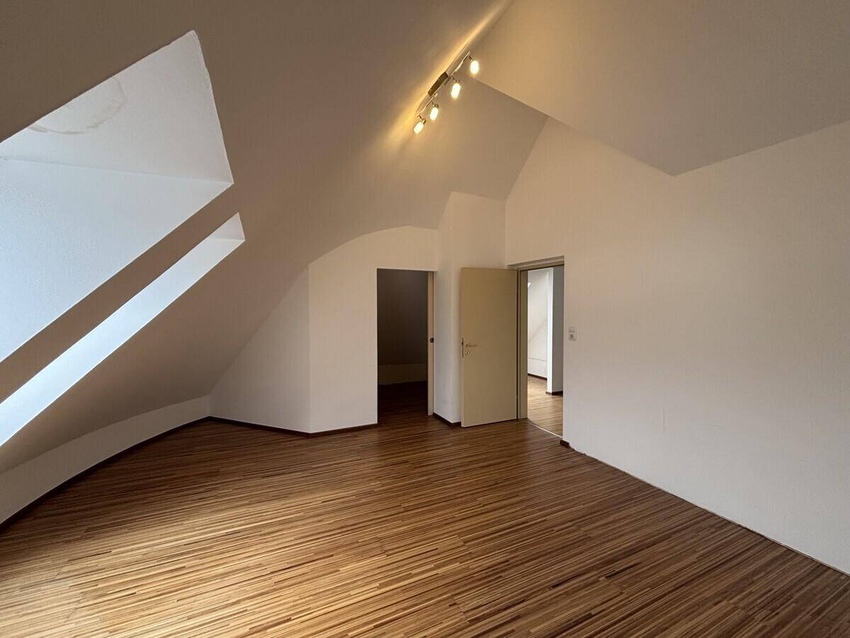 Helles Dachgeschosszimmer mit Holzfußboden, Dachfenstern und Deckenstrahlern.