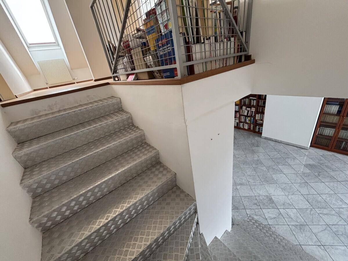 Metalltreppe führt zu einem oberen Bereich mit Bücherregalen und Dachfenster.