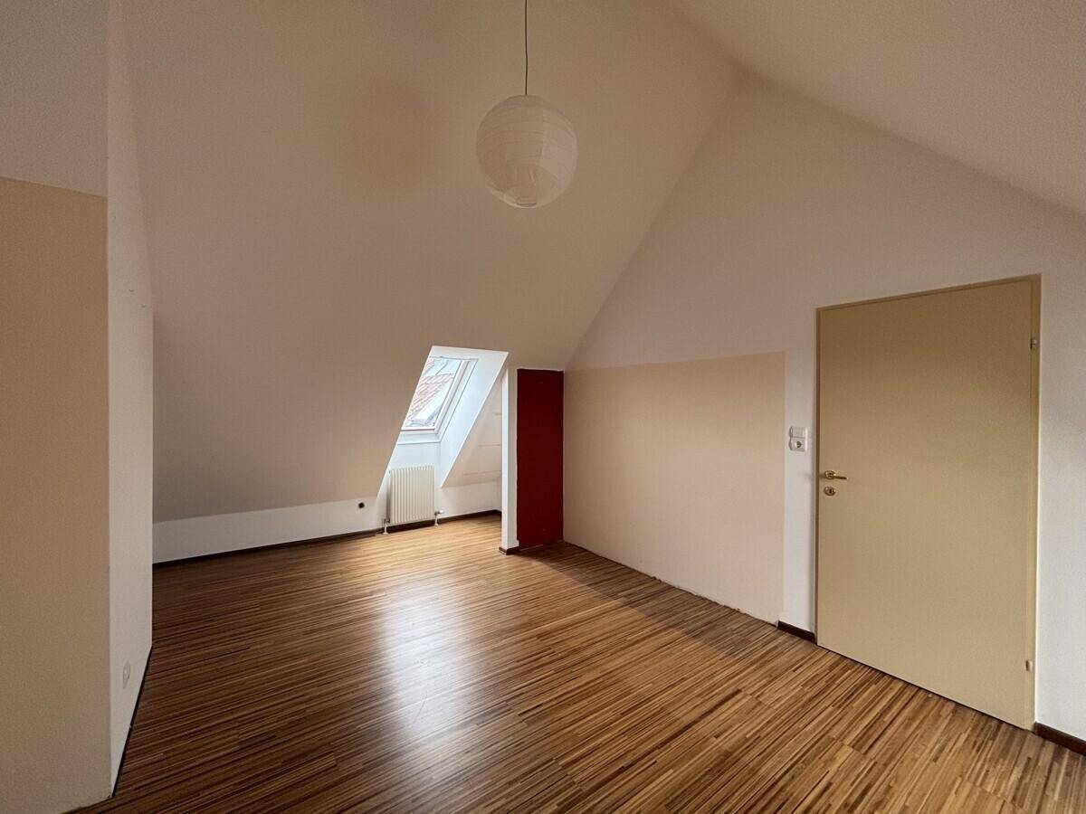 Dachgeschosszimmer mit Holzfußboden, Dachfenster und hellen Wänden.