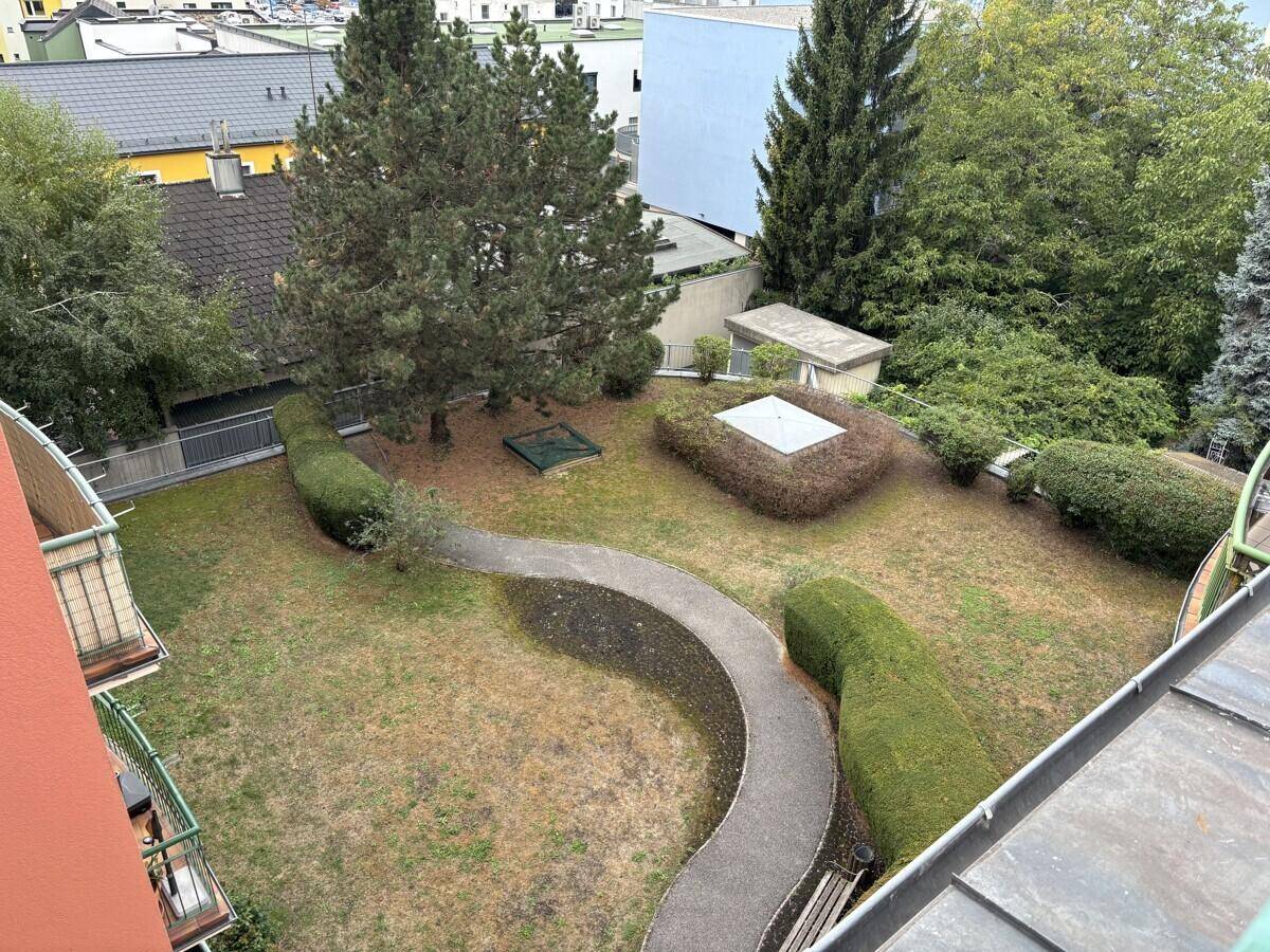 Gemeinschaftsgarten mit geschwungenem Weg, gepflegten Hecken und Bäumen, umgeben von Wohngebäuden.