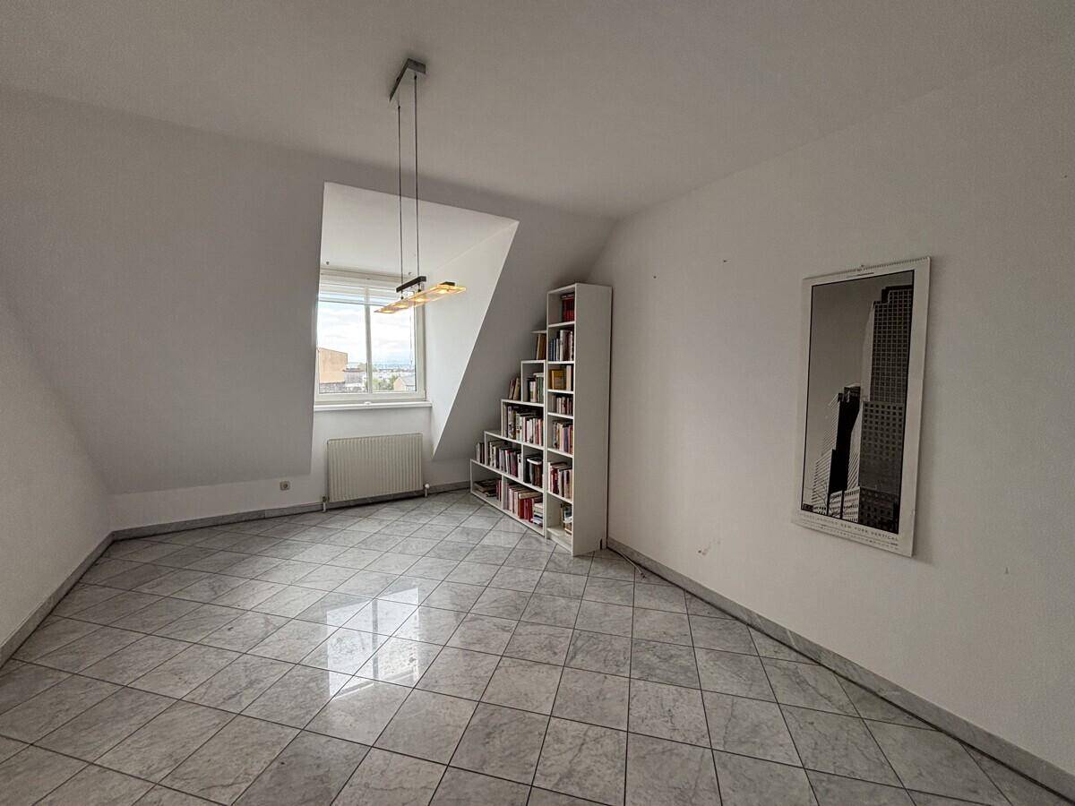 Dachgeschosszimmer mit schrägen Wänden, Fenster und Fliesenboden.