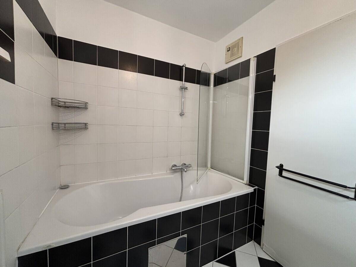 Badezimmer mit Badewanne, Duschabtrennung und schwarz-weißen Fliesen.