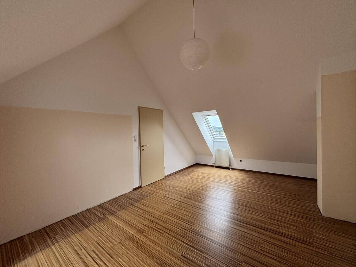 Geräumiges Dachgeschosszimmer mit Holzfußboden, Dachfenster und hellen Wänden.