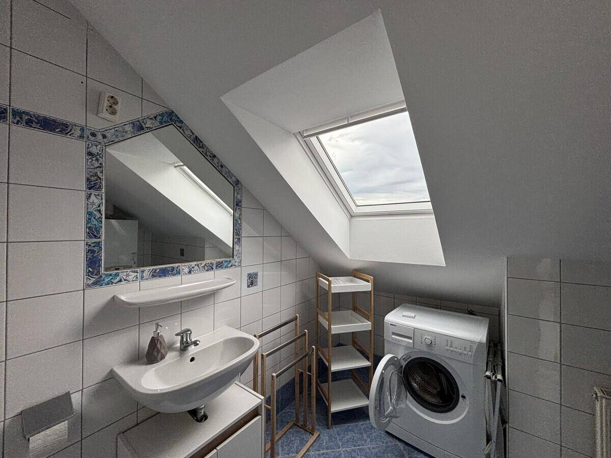 Badezimmer mit blauen und weißen Fliesen, Waschbecken, Waschmaschine und Dachfenster.
