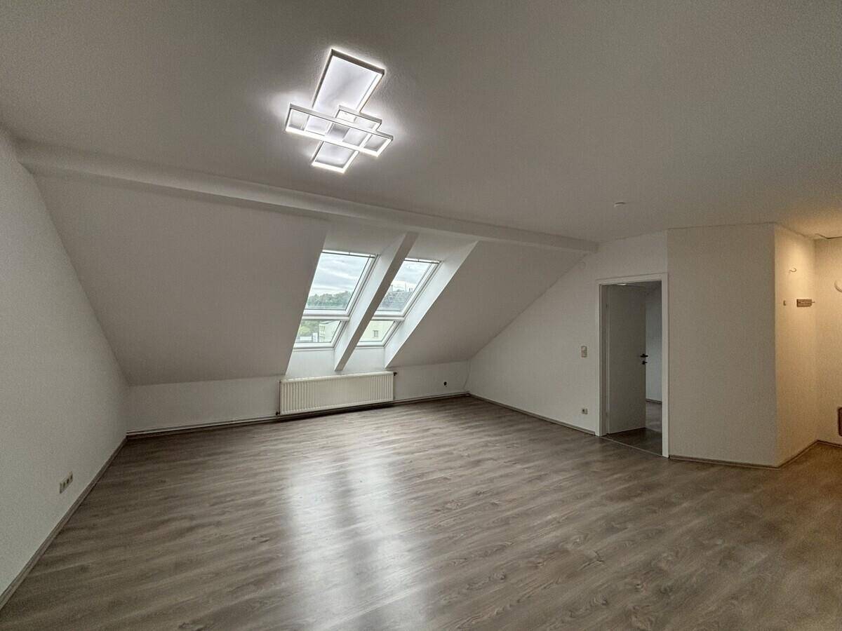 Heller Wohnraum im Dachgeschoss mit Laminatboden, Dachfenstern und Heizkörper.