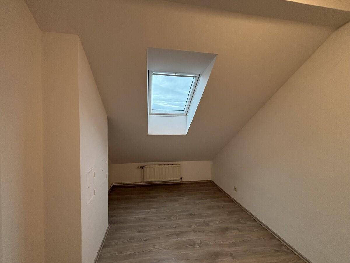 Gemütliches Zimmer im Dachgeschoss mit Laminatboden, Dachfenster und Heizung.