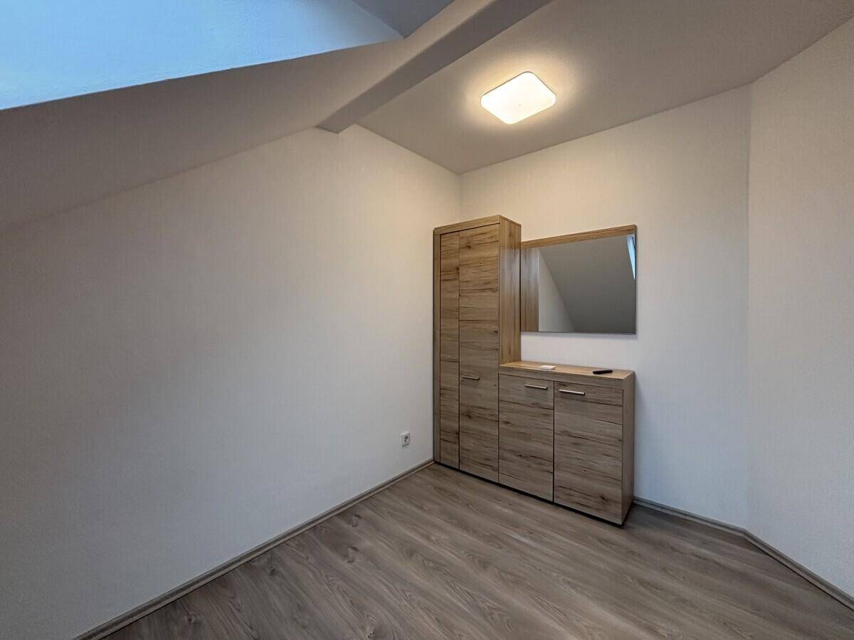 Schlafzimmer mit Laminatboden, Dachschrägen und einem modernen Holzschrank mit Spiegel.