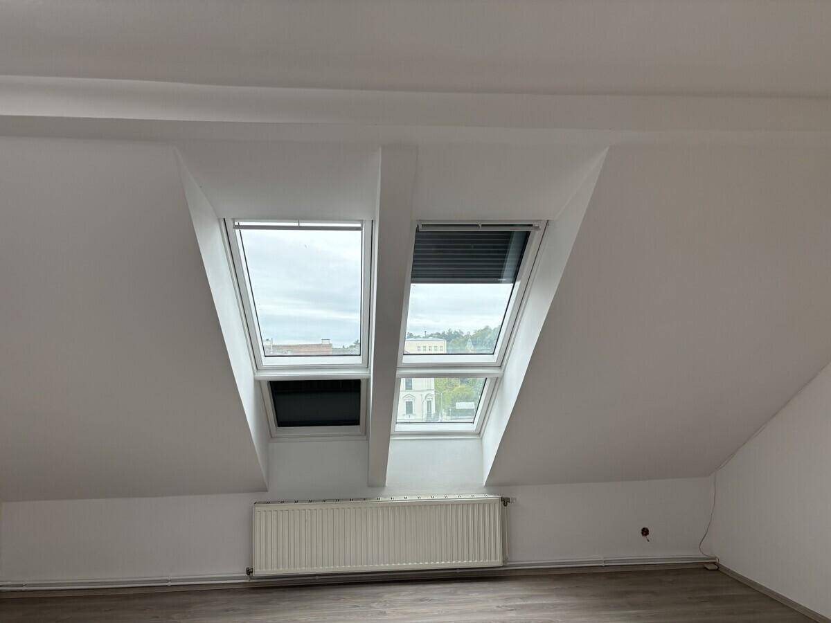 Zwei Dachfenster mit Blick nach draußen und einem Heizkörper darunter.