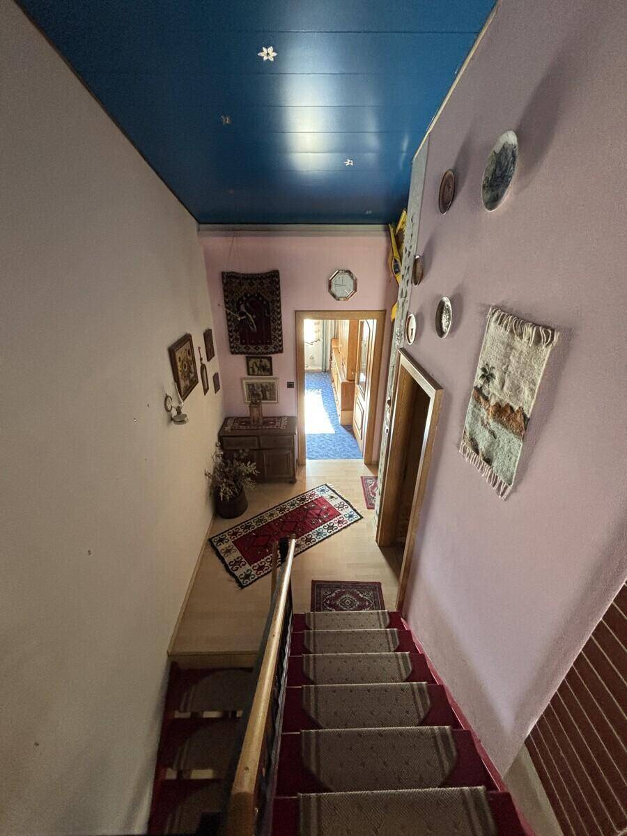 Flur mit rosa Wänden, blauer Decke und Treppe, geschmückt mit traditionellen Wandteppichen.