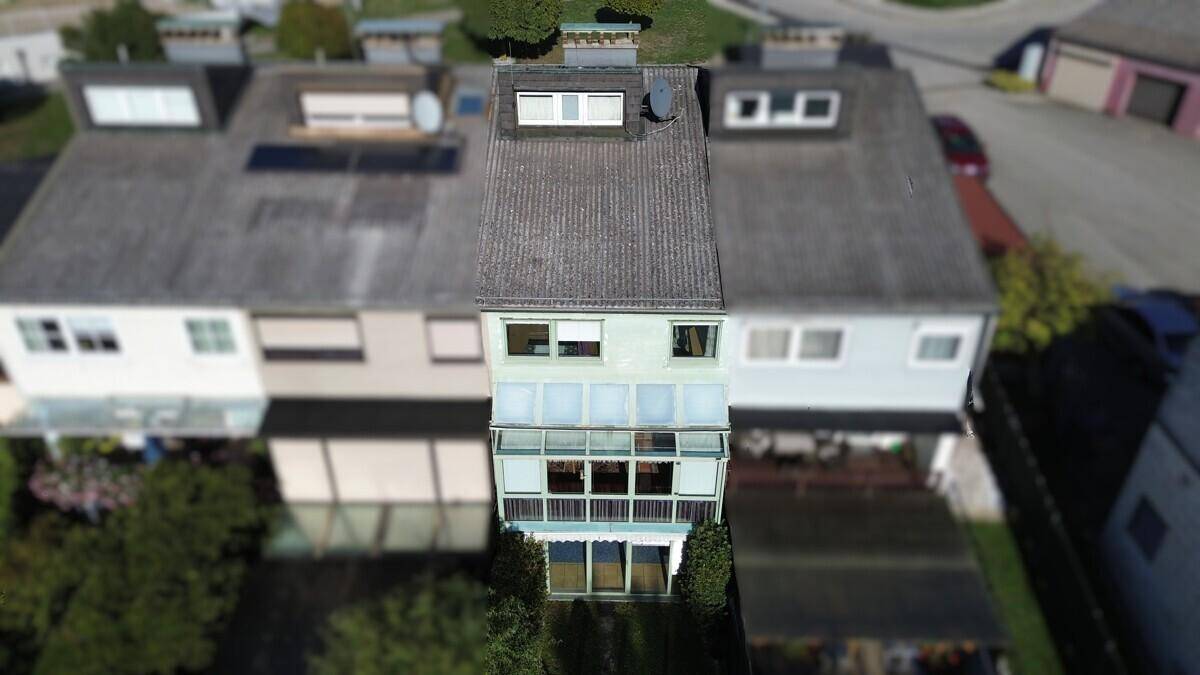 Rückansicht eines Reihenhauses mit Wintergarten und Dachfenstern unter blauem Himmel.